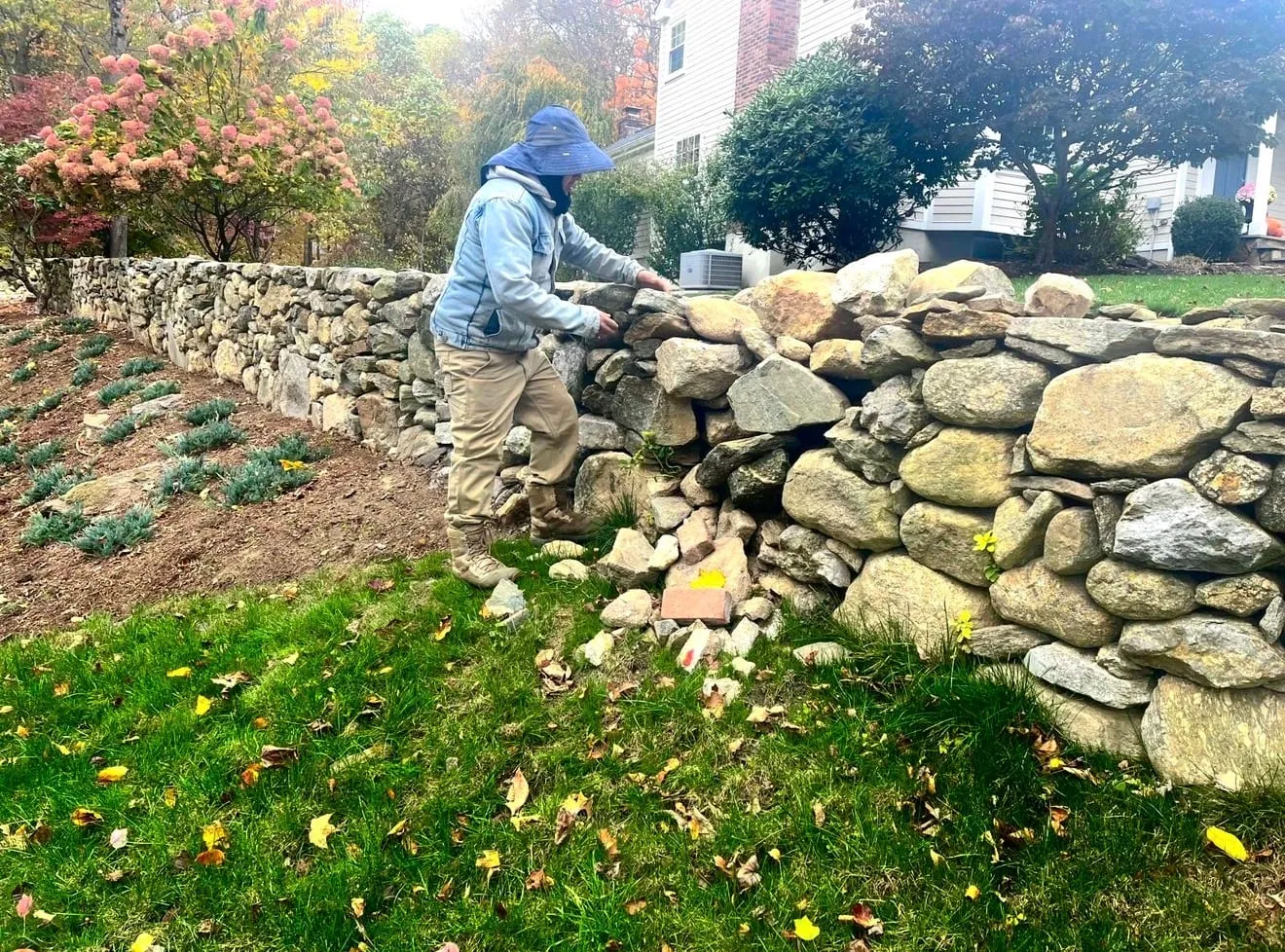 MRO mason rebuilding a natural fieldstone retaining wall by hand